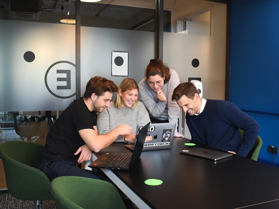 Four colleagues gathered around a laptop in a meeting room.